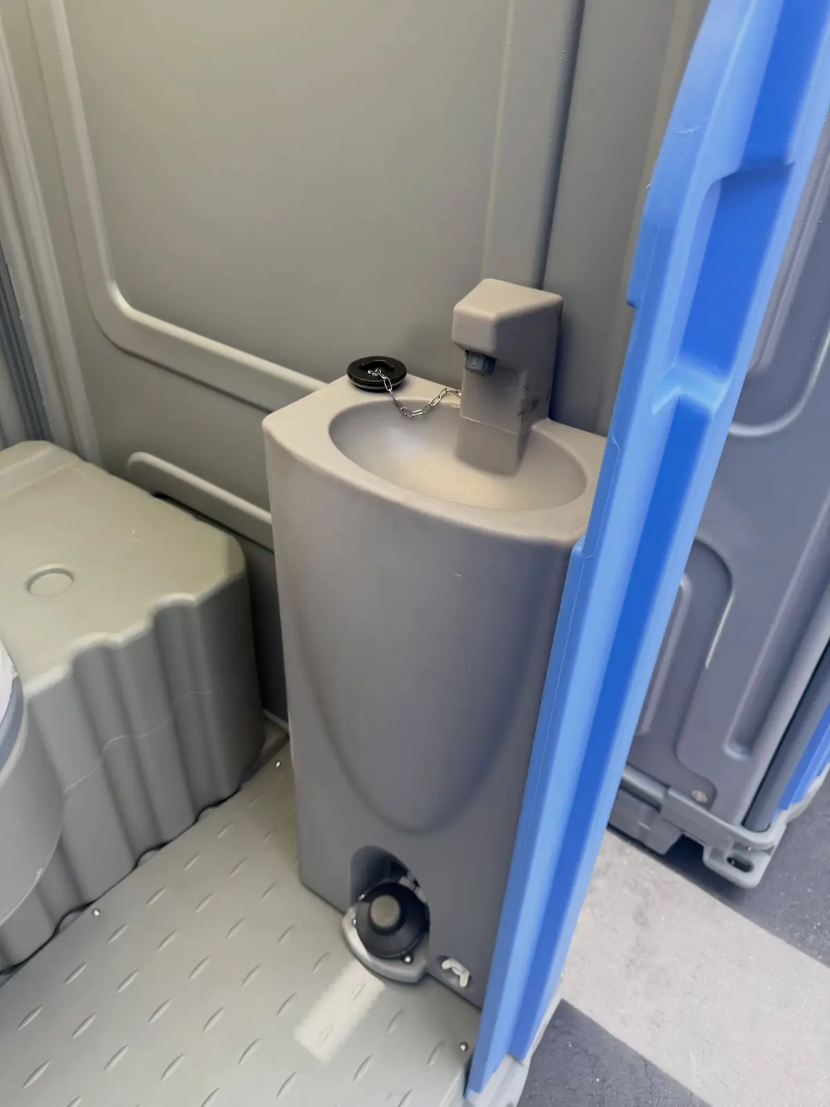 Inside a deluxe portable toilet with a pedestal hand sink beside the seat