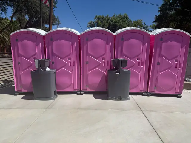 Pink porta potties lined up with gray hand washing stations between them