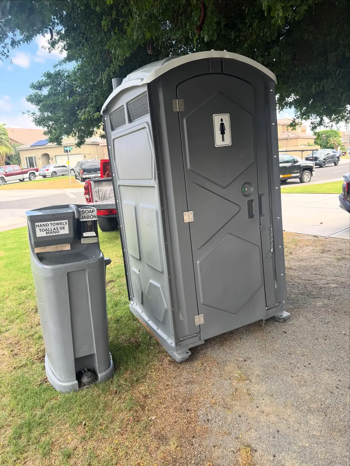 Gray porta potty with a hand washing station on a lawn