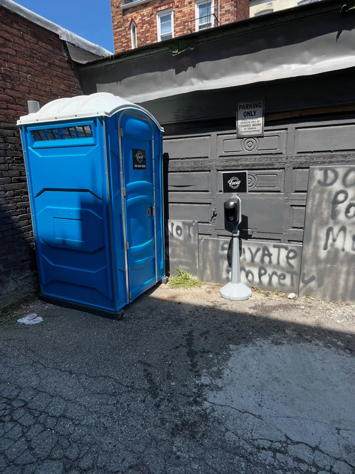 A blue porta potty set beside a house on pavement